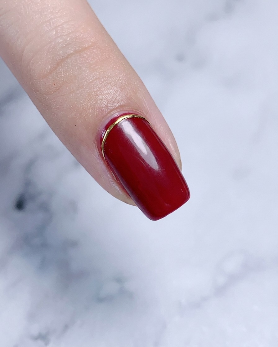 An index finger featuring a elegant gold accent piece placed at the cuticle line.