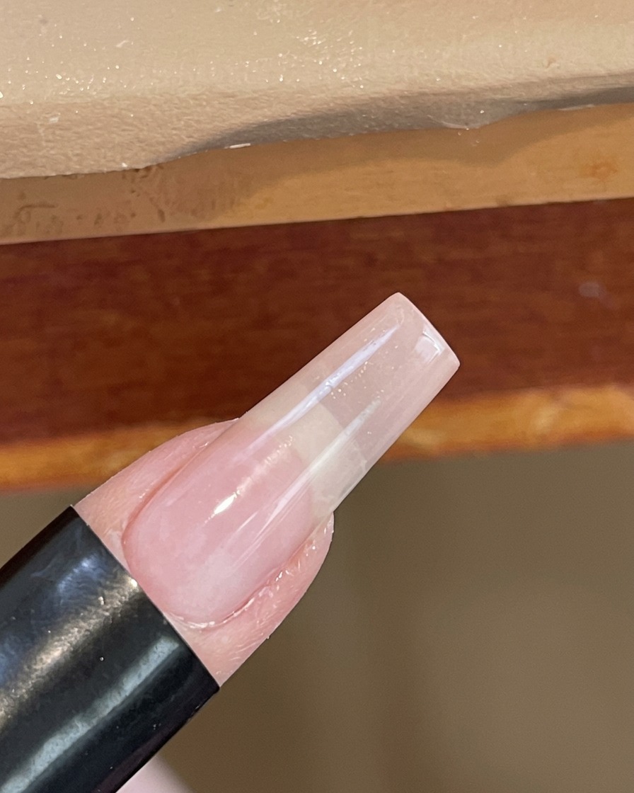 A close-up view of a nail being cured under a small, handheld white UV/LED lamp.
