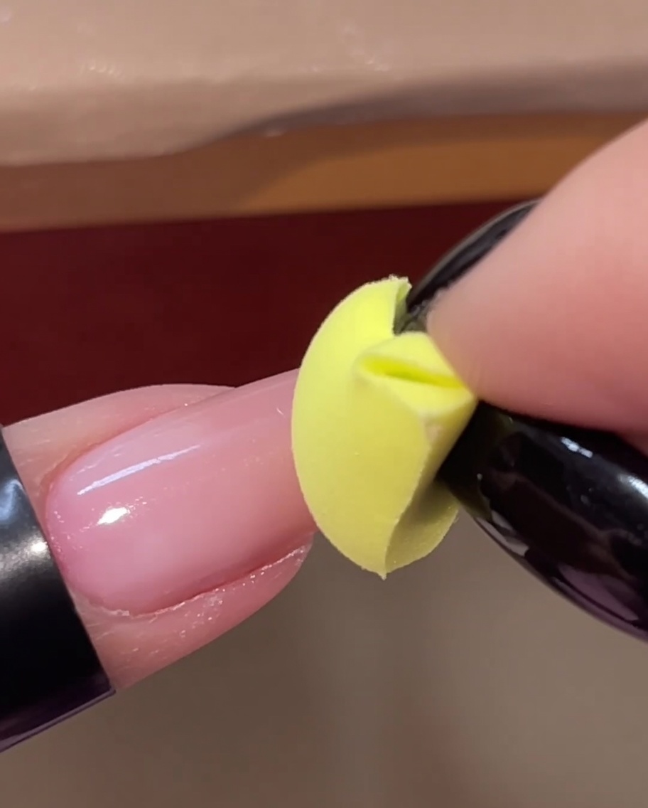 A yellow sponge wedge patting a second layer of pink gel onto the tip of a nail.