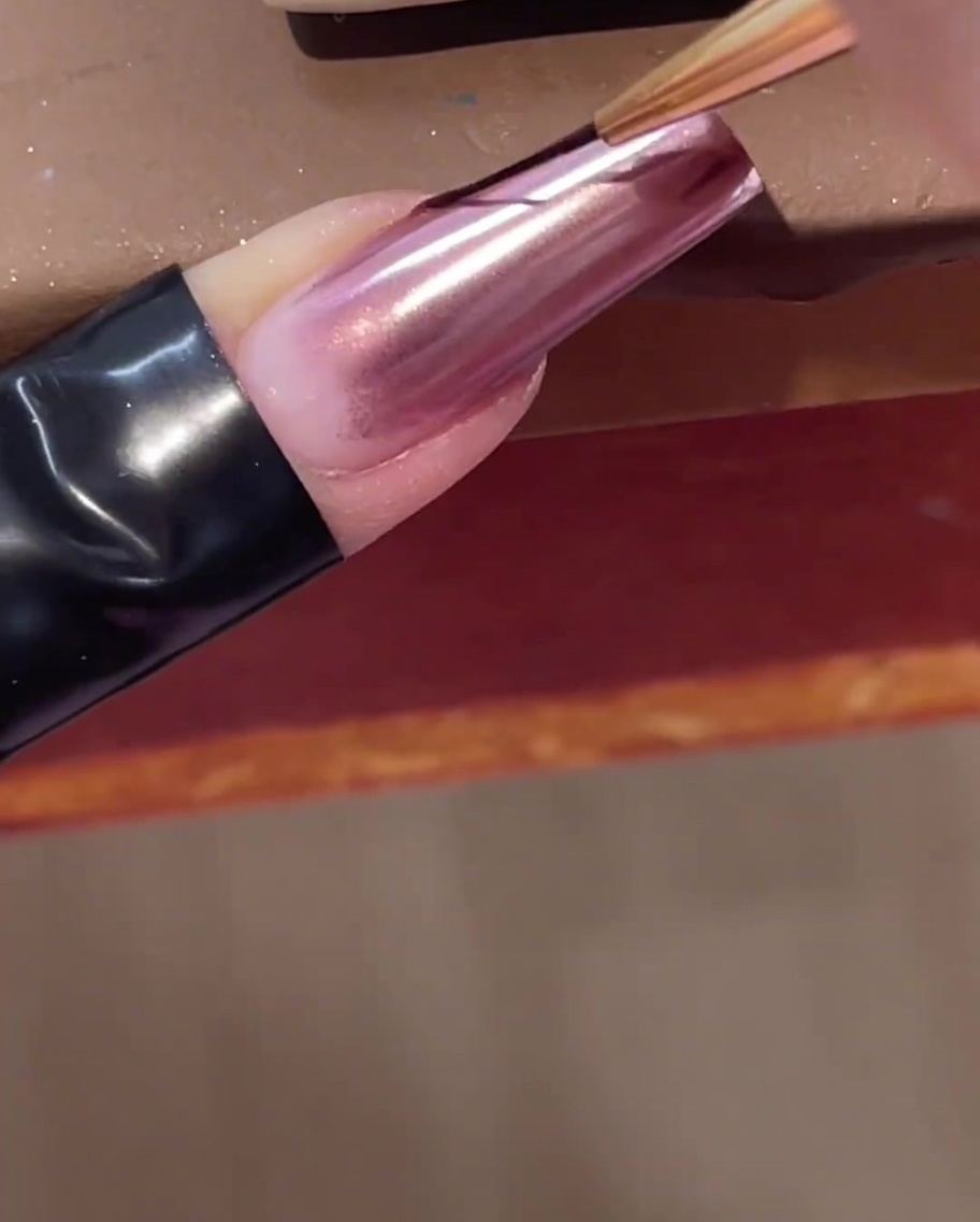 A thin nail art liner brush applying a clear line of builder gel diagonally across a chrome nail.