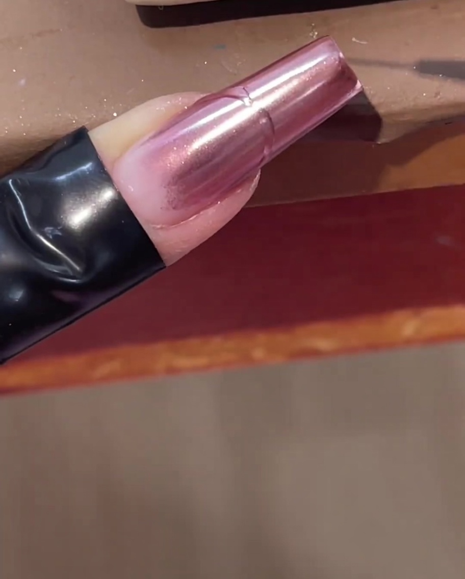 A fine liner brush drawing a raised clear gel line over a pink chrome nail.