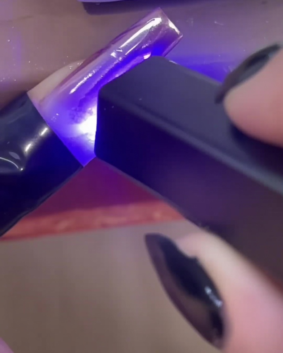 A mini handheld UV/LED lamp curing clear 3D builder gel lines on a nail extension.