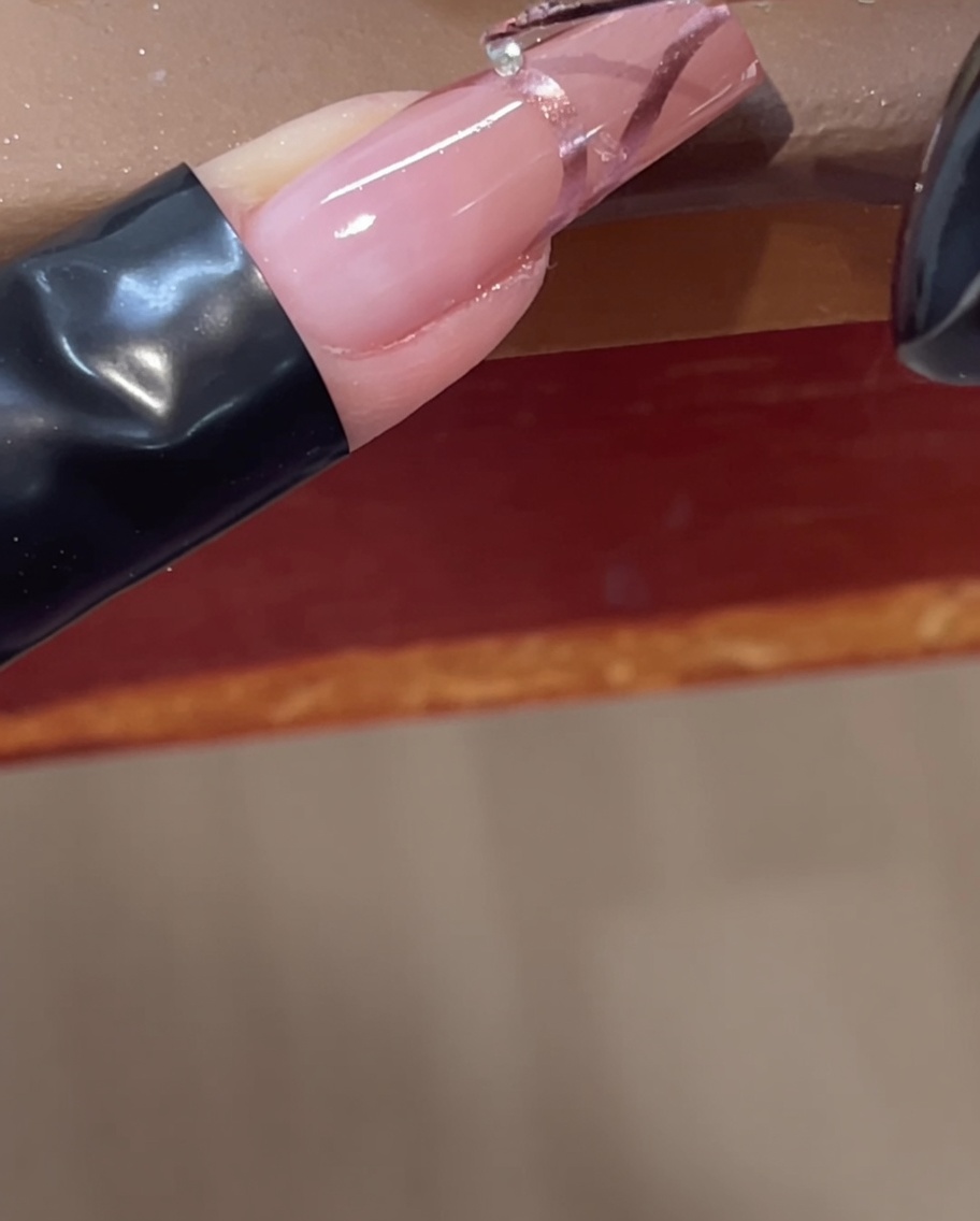 Placing a small clear rhinestone onto a 3D chrome line on a pink nail using a tool.