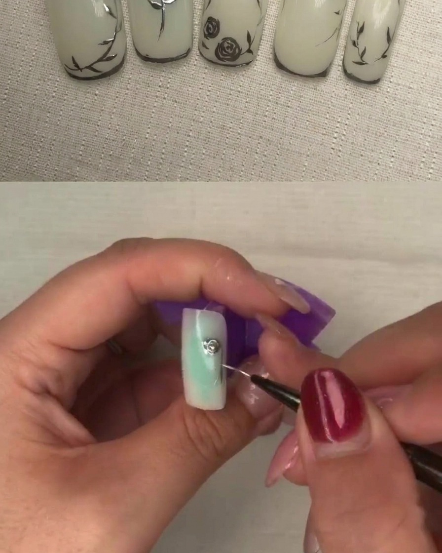 A close-up of a liner brush applying thick metallic gel to the center of a petal design on a white base nail.