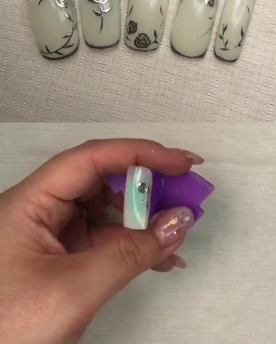 A close-up view of the completed metallic rose petal design on a white nail, showing detailed texture.