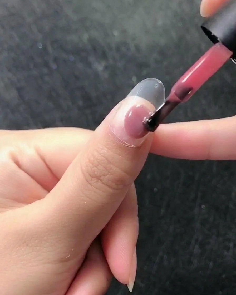 Close-up of a brush applying a sheer pink gel polish to a natural, prepped nail.