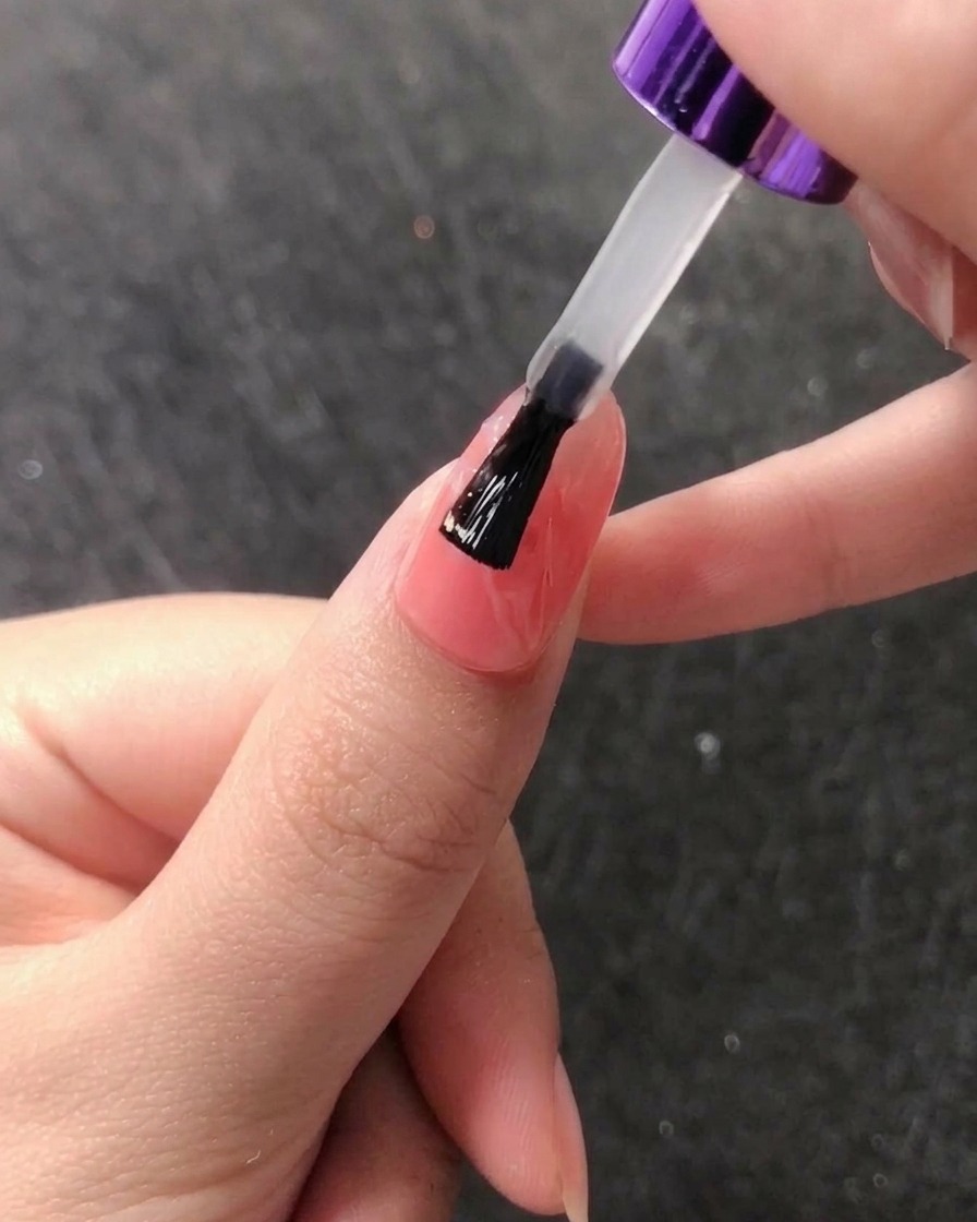 A sponge applicator rubbing rose gold chrome powder onto a nail to create a mirror-like finish.