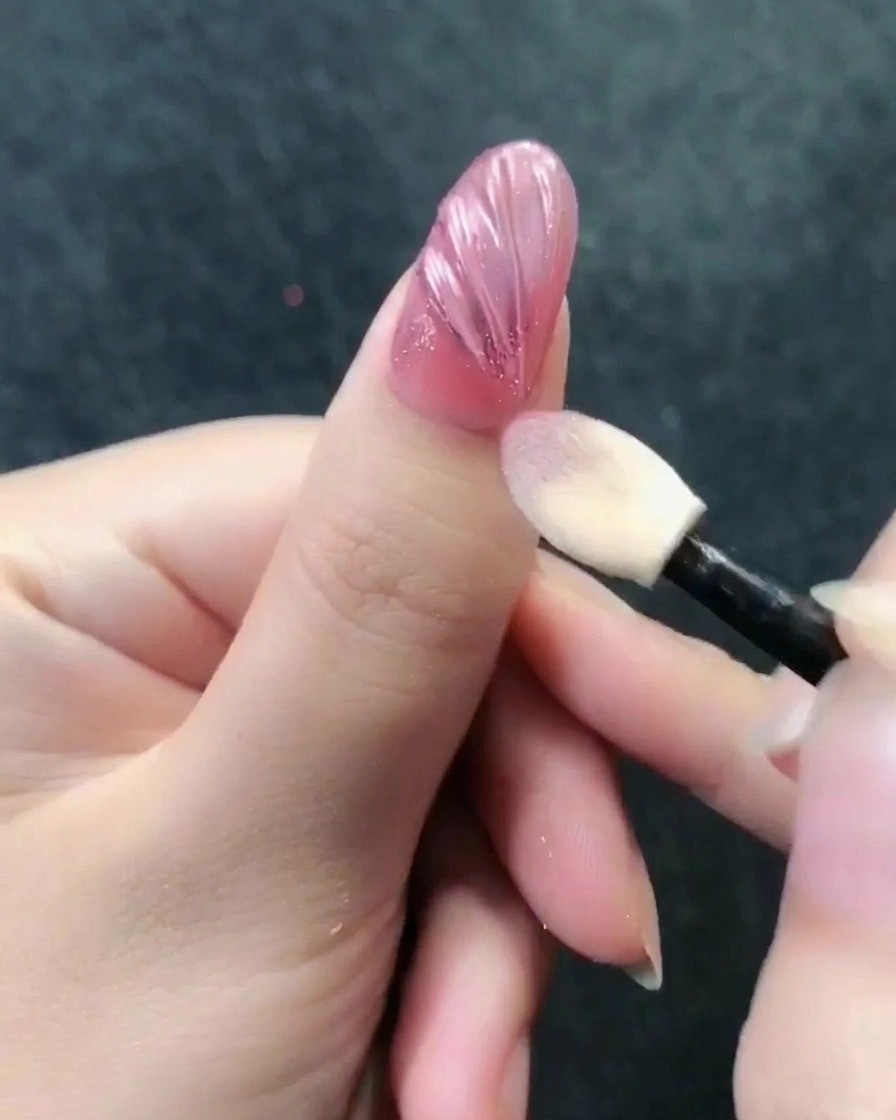 An eyeshadow applicator buffing rose gold chrome powder onto a textured nail surface.
