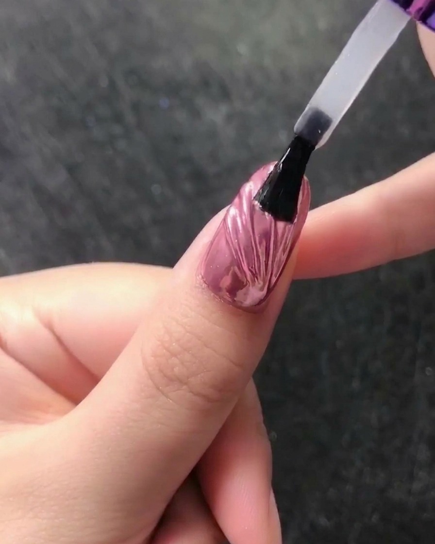 A close-up of a wax pencil placing a small white pearl at the base of a chrome-finished nail.