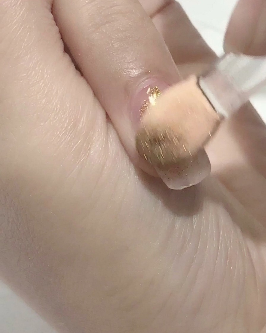 A brush applying clear top coat over a pink gel nail.