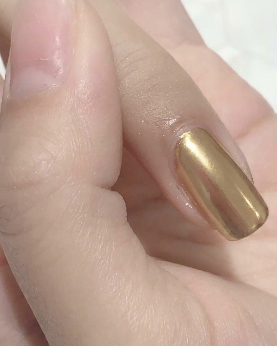 A sponge applicator buffing gold mirror powder onto a nail.