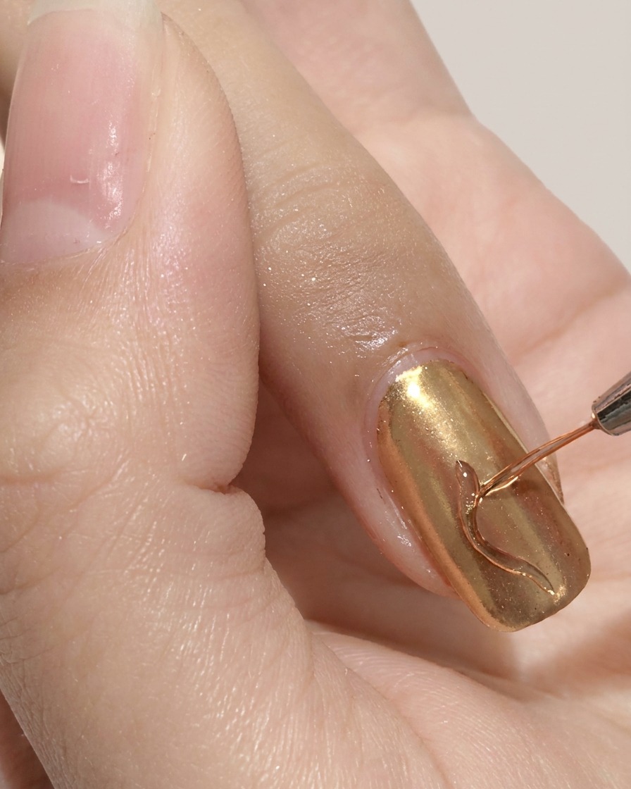 A fine liner brush drawing a wavy line on a gold chrome nail.