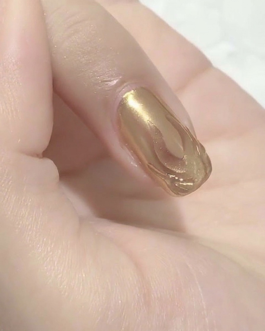 A close-up view of a wet cotton pad wiping over a nail surface, revealing the defined metallic flame pattern beneath.
