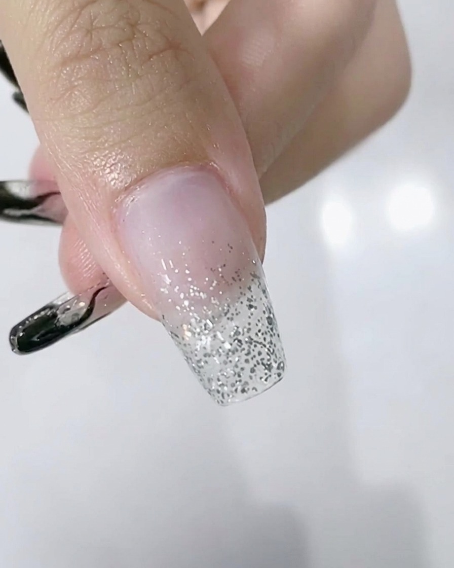A close-up of a hand with a silver glitter gradient on the nails positioned inside an LED lamp.
