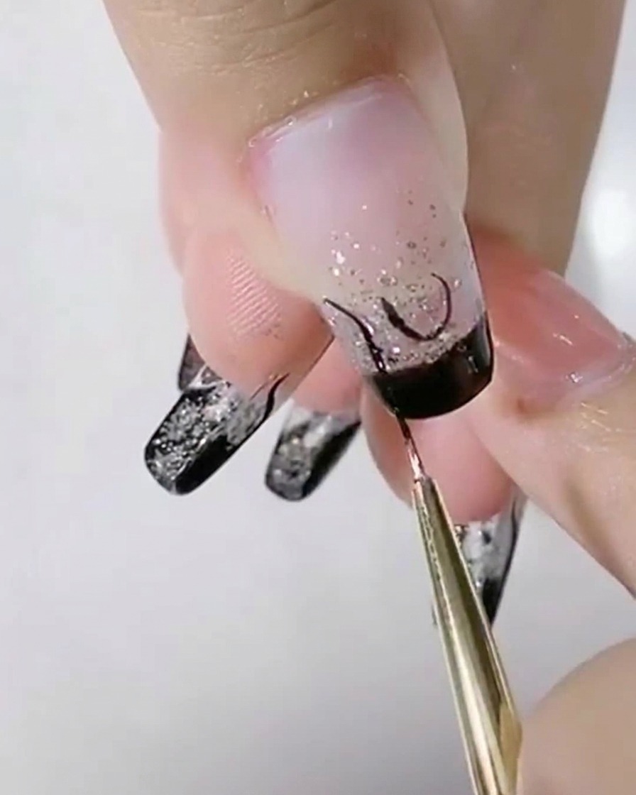 A liner brush adding black S-shaped curves next to a central U-shape on a silver glitter nail.