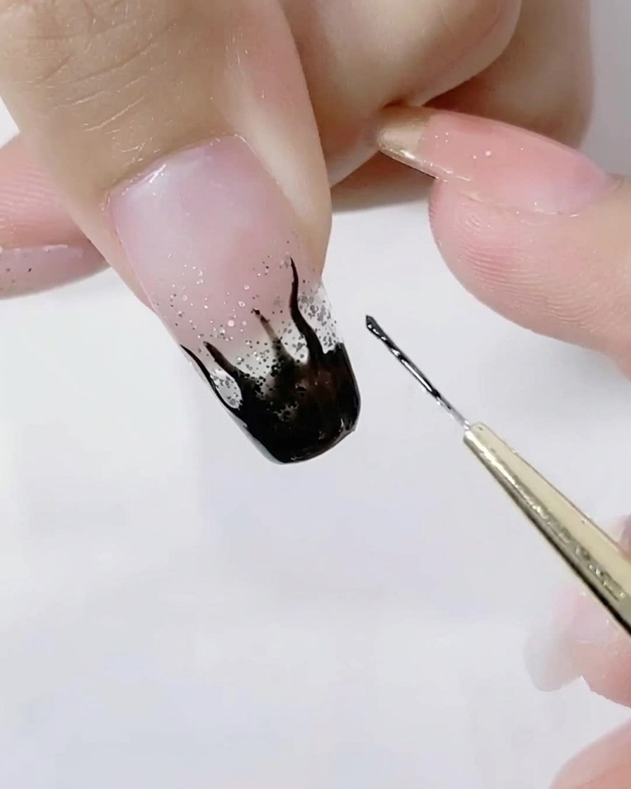Close-up of a liner brush detailing the sharp points of black flames on a glitter nail.