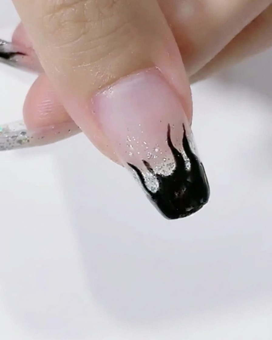Nails with black flame art curing under the bright light of an LED lamp.