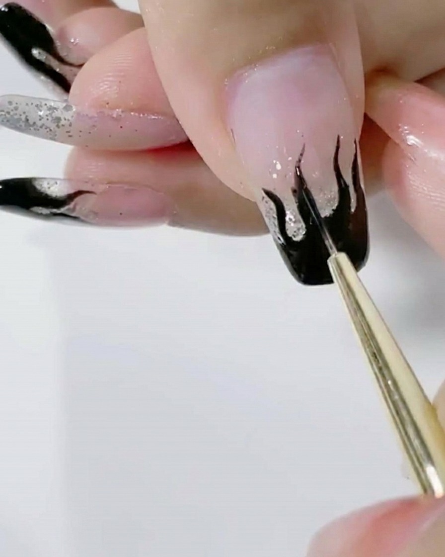 A liner brush applying a second coat of saturated black gel to the flame art on a glitter nail.