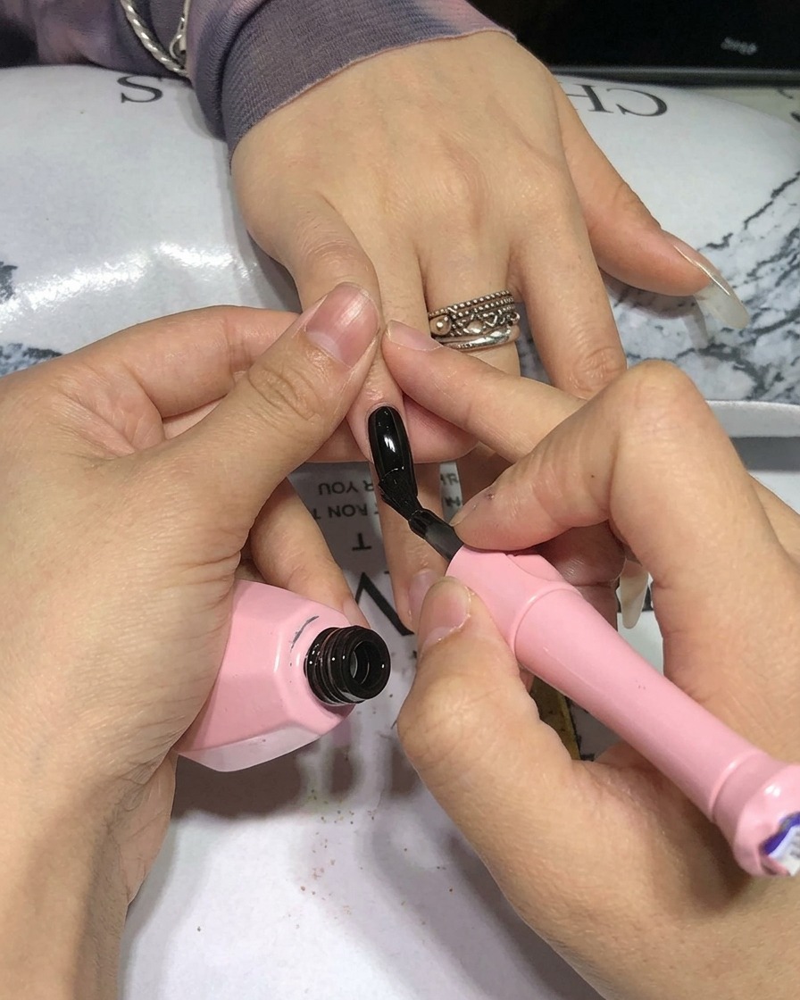Close-up of a brush applying black gel polish onto a natural nail.