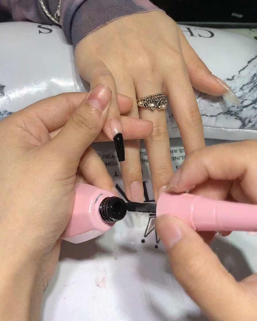 A brush applying a second coat of black gel polish to the nail, showing deep saturation.