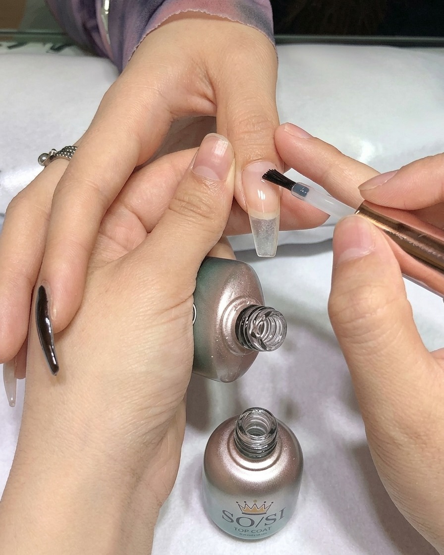 A brush applying clear top coat over a black painted nail.