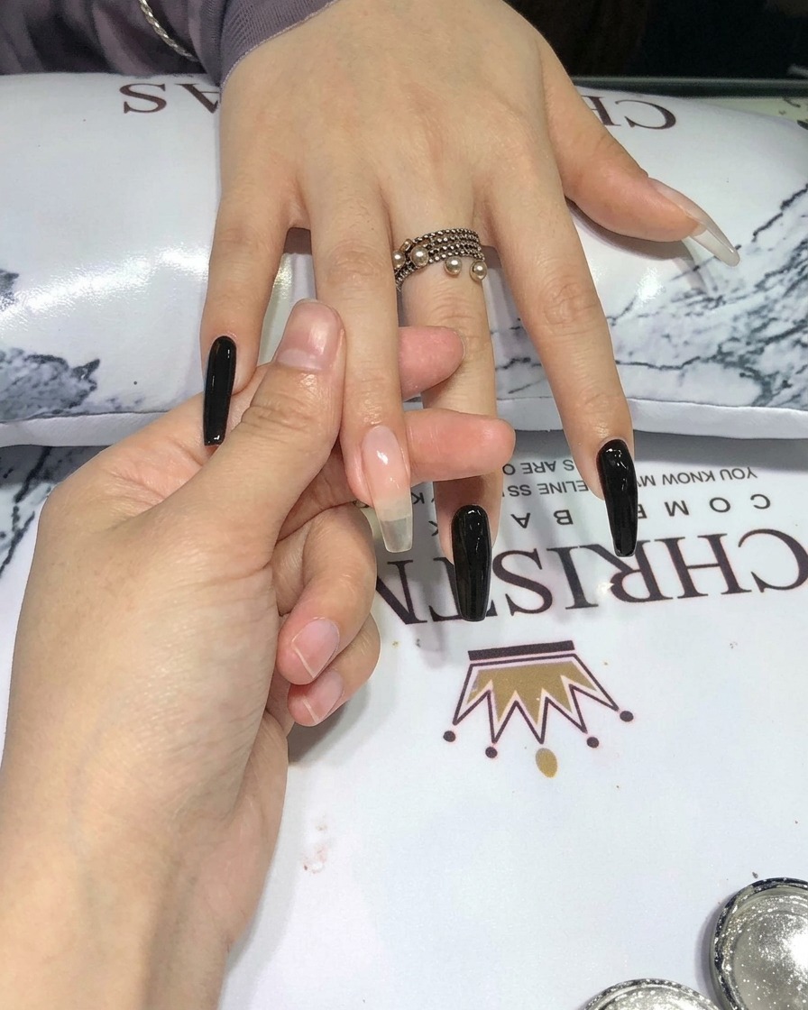 A silicone applicator pressing silver chrome powder onto a black nail surface.