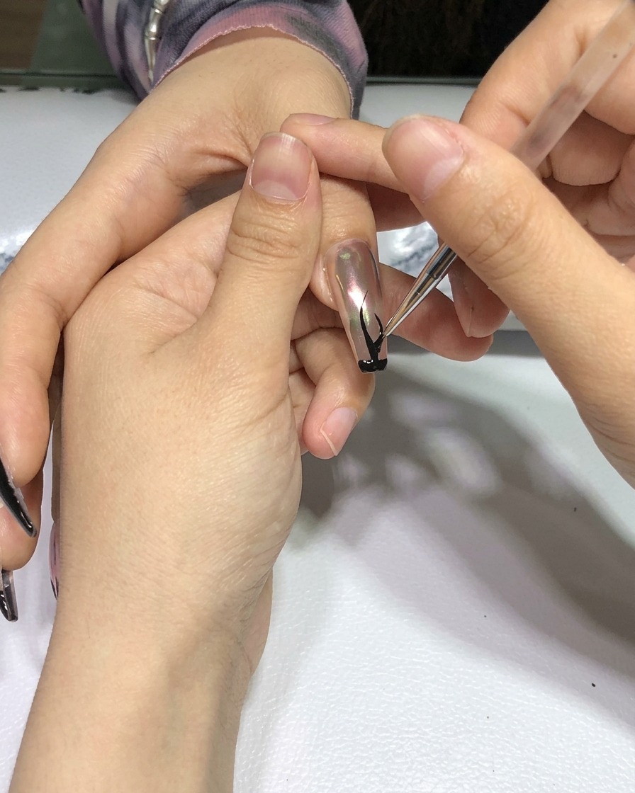 A hand with the completed black flame nail art positioned inside a professional nail curing lamp.