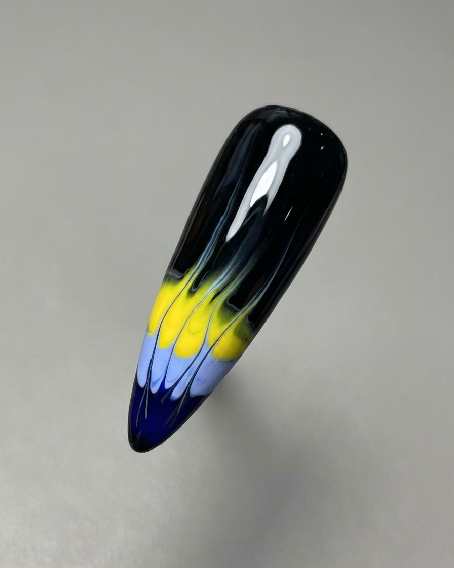 A thin nail liner brush dragging the blue and yellow gel colors upward to create the base of the flame pattern.