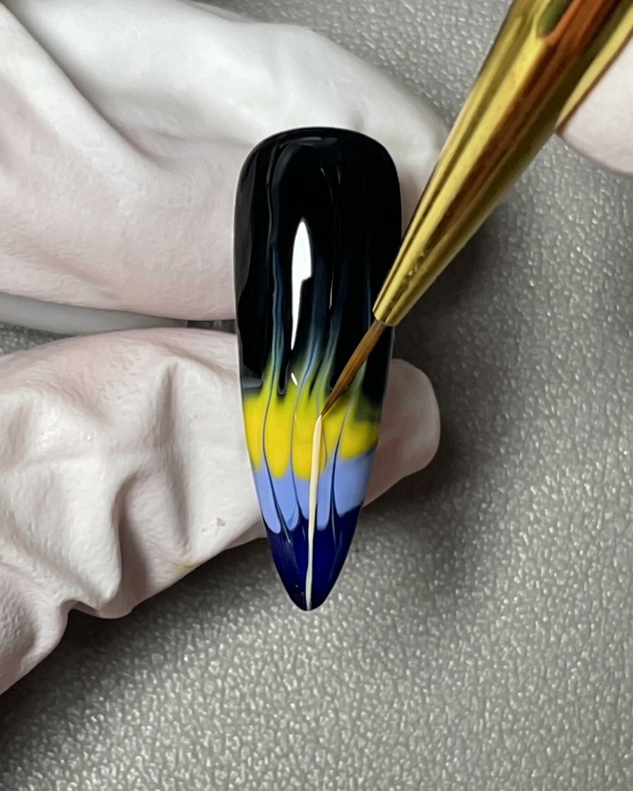 A close-up of a nail brush pulling thin lines from the colored flame shapes toward the cuticle area.