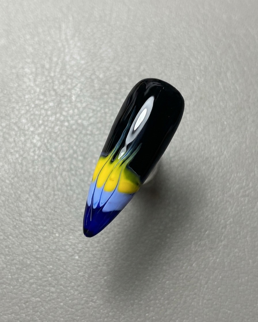 A brush applying a layer of clear glossy gel top coat over the finished flame nail art.