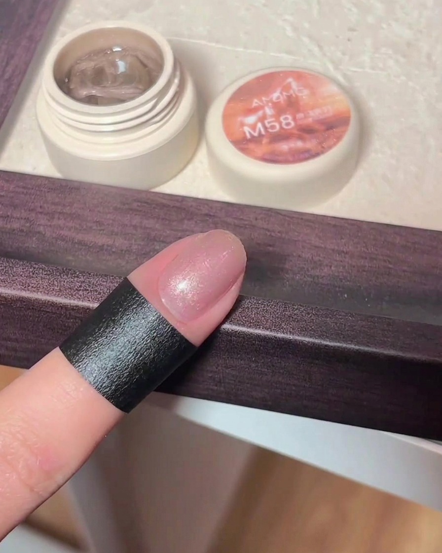 A hand holding a magnetic wand over a freshly applied cat eye gel nail, showing the shimmering particles shifting into a cat eye pattern.