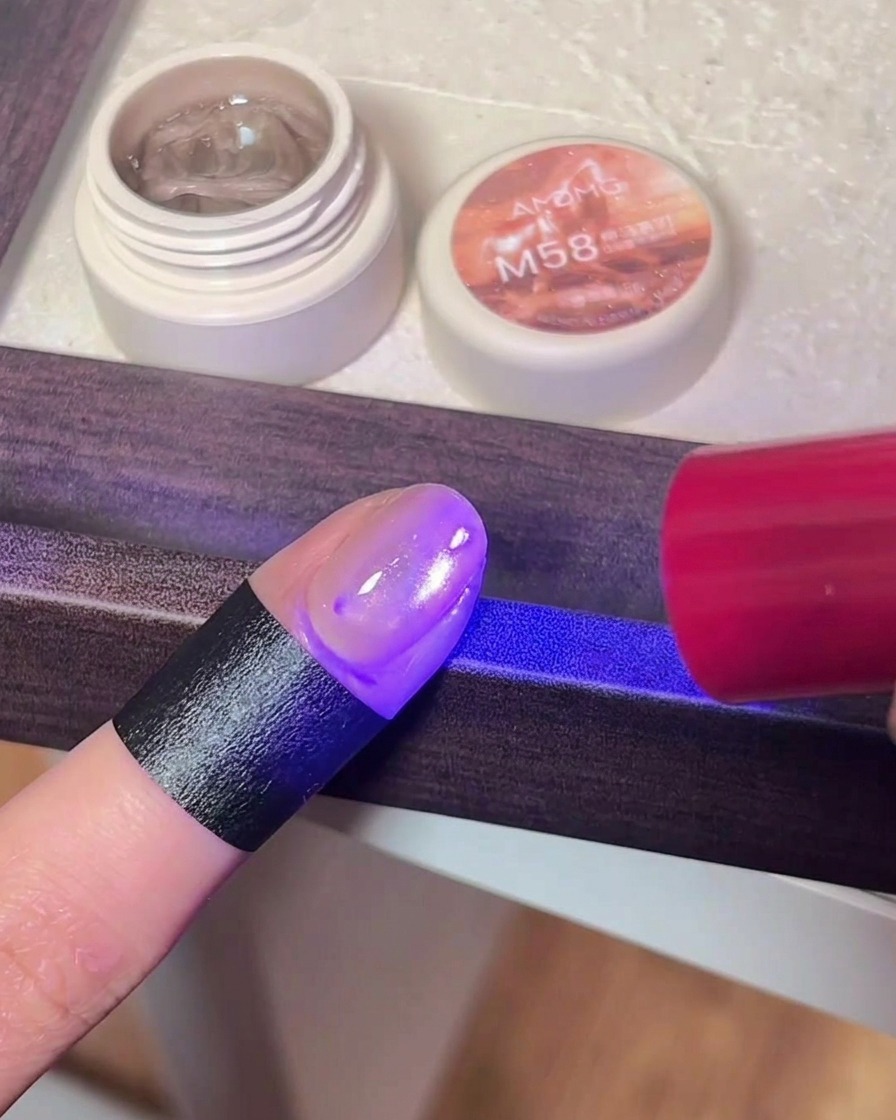A close-up of a finger with cat eye gel polish placed under the purple light of a UV/LED nail lamp.