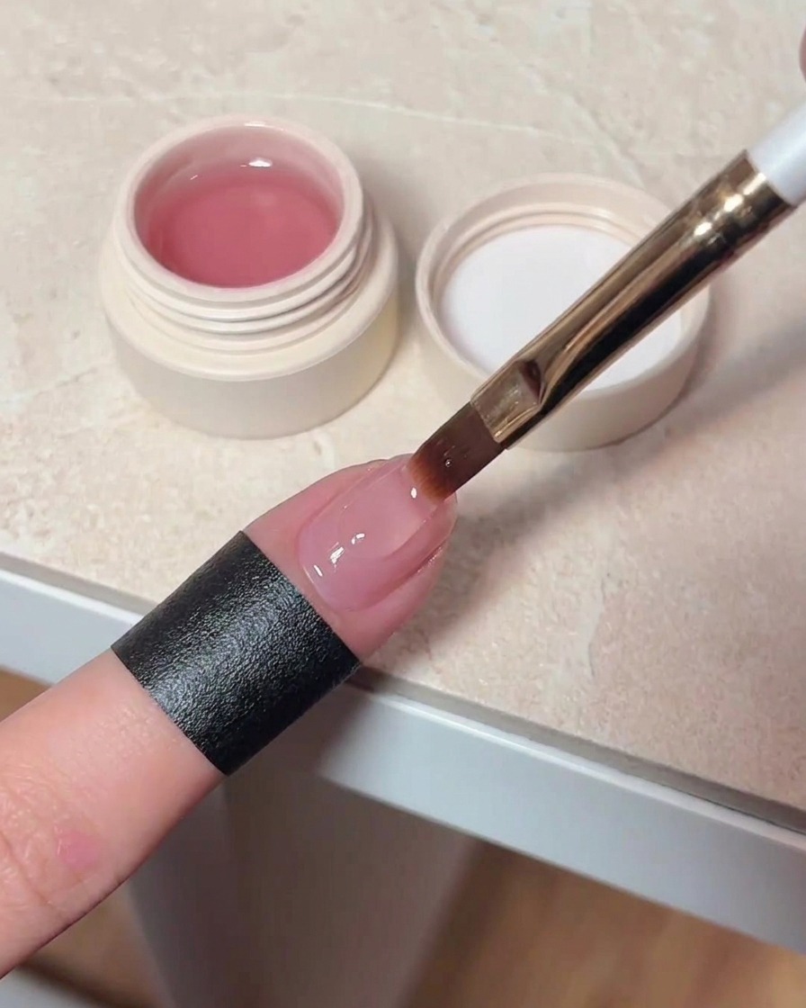 A nail brush applying a clear, glossy top coat over a cured cat eye nail.