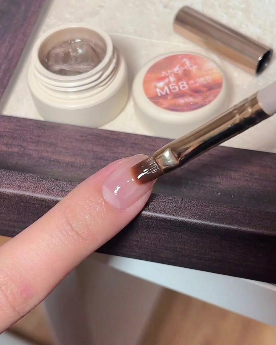 Tweezers placing a small, shiny star-shaped glitter piece onto a nail covered in wet, clear gel top coat.