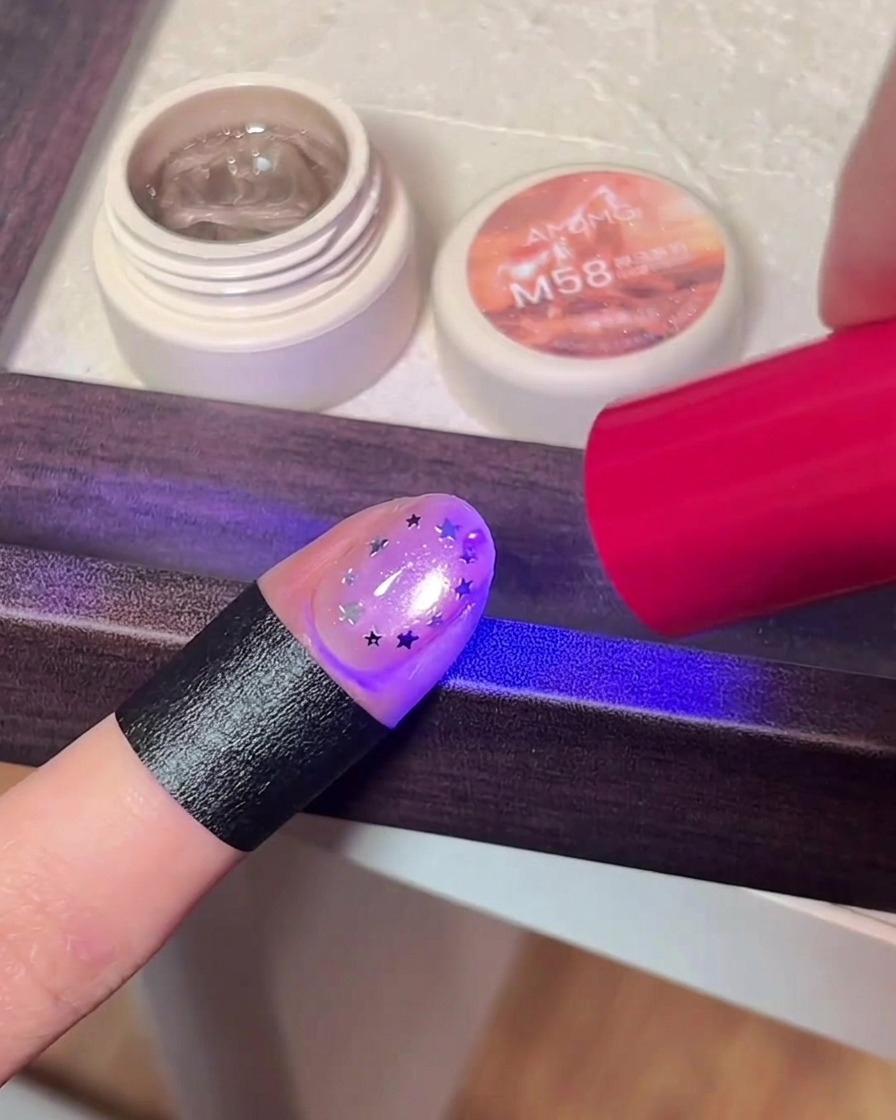A finger with star glitter art being cured under the purple light of a UV/LED lamp.