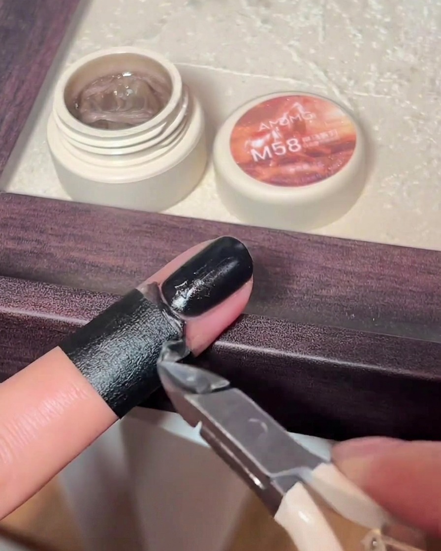 A small nail art brush painting black gel polish over a raised cross charm on a fingernail.