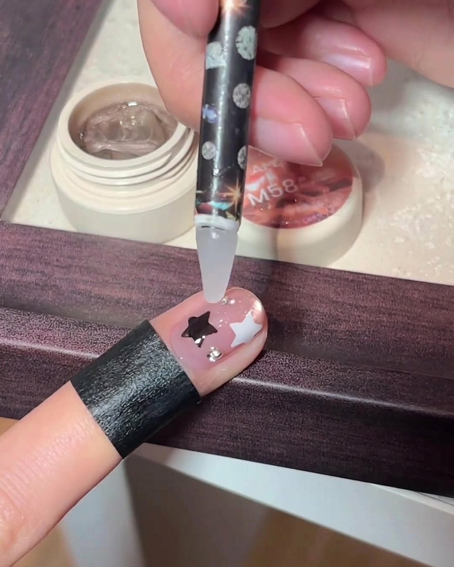 A precision tool placing tiny rhinestones onto a decorated fingernail.