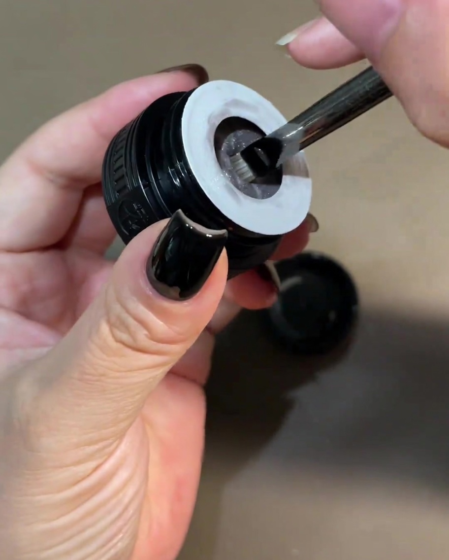 A small brush dipping into a jar of pearlescent white cat-eye gel.