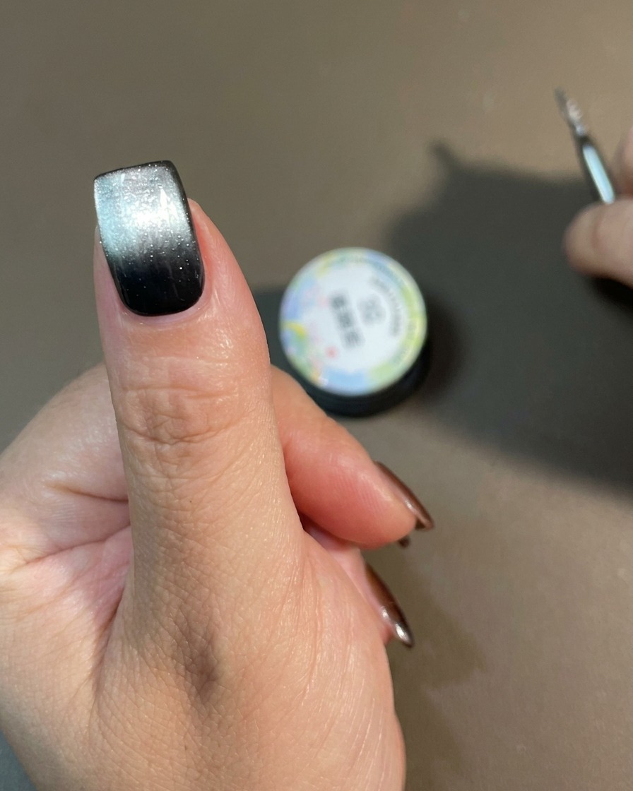 A hand with a finished cat-eye gradient design curing inside a nail lamp.