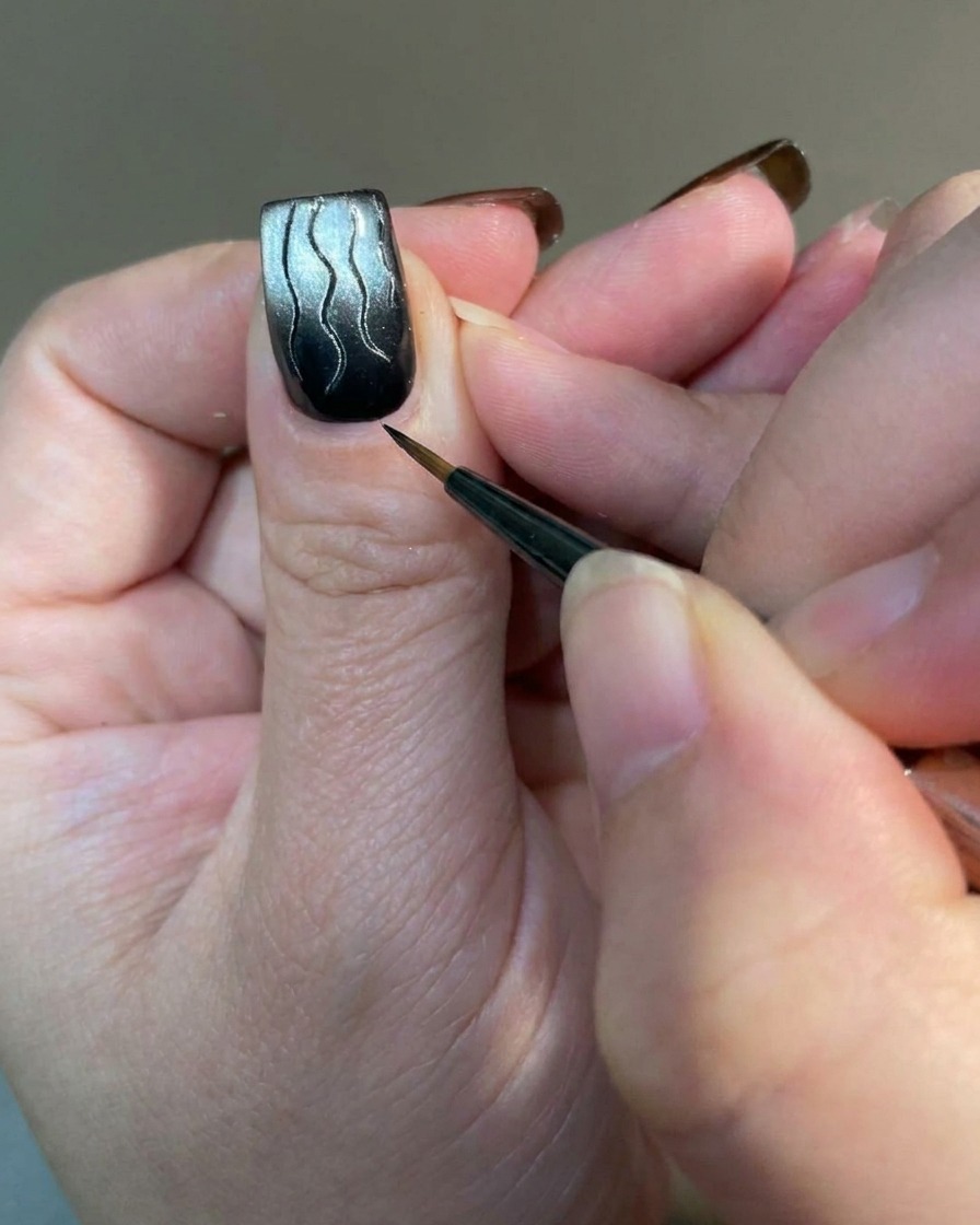 A macro shot of a liner brush adding small, delicate accent lines to the base of a flame-designed nail.