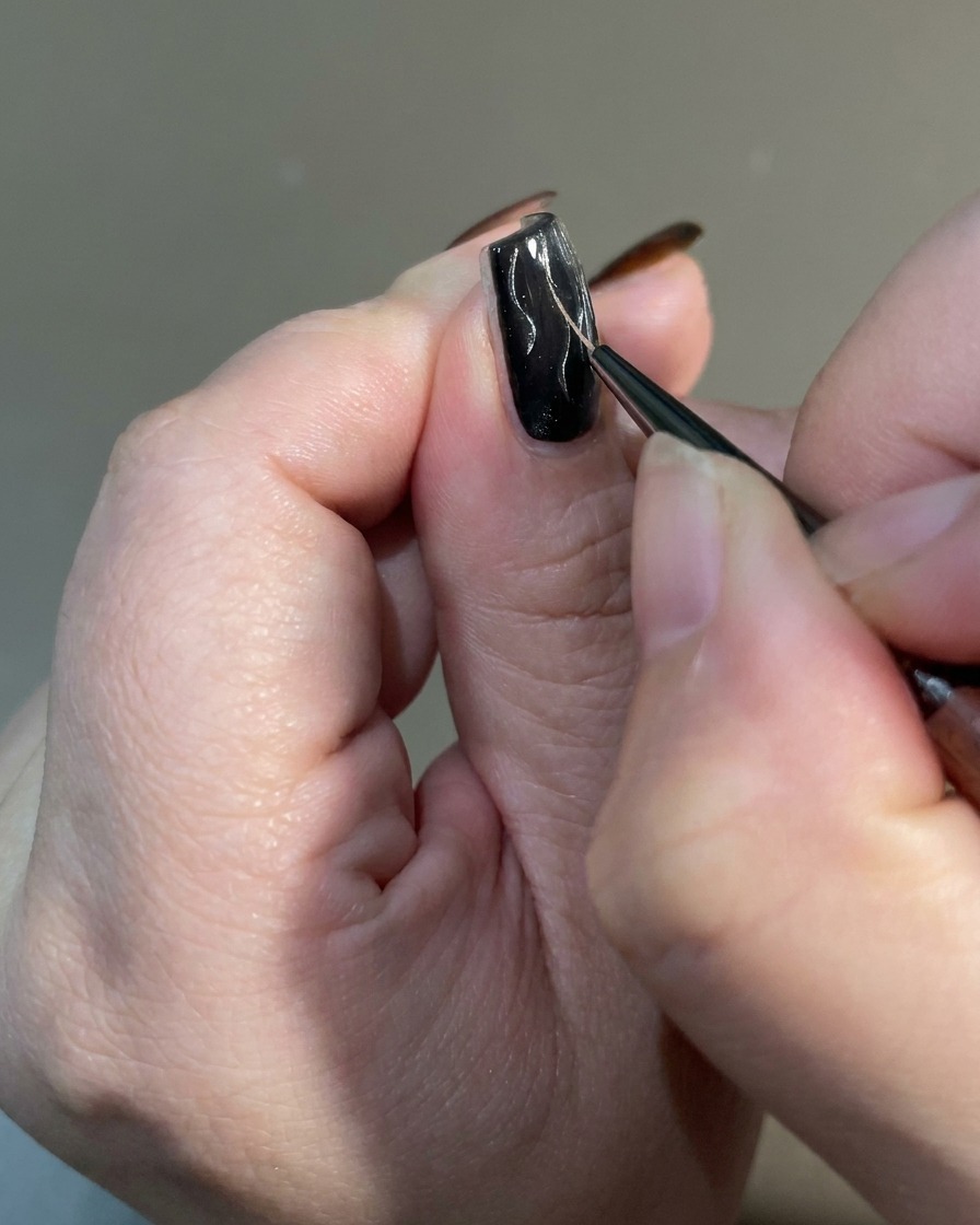 A close-up of a liner brush tapering the ends of flame designs on a nail to create a sharp, irregular finish.