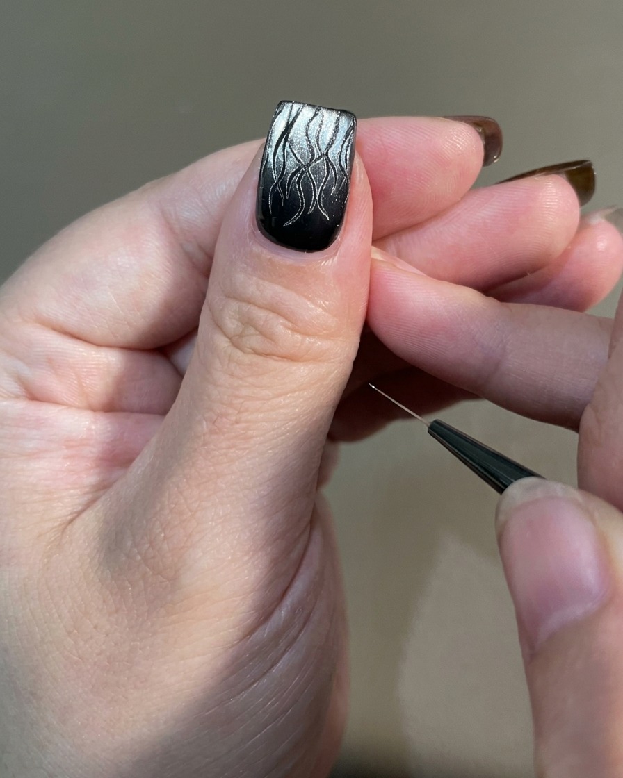 A hand with finished flame nail art being placed under a professional UV nail lamp for curing.