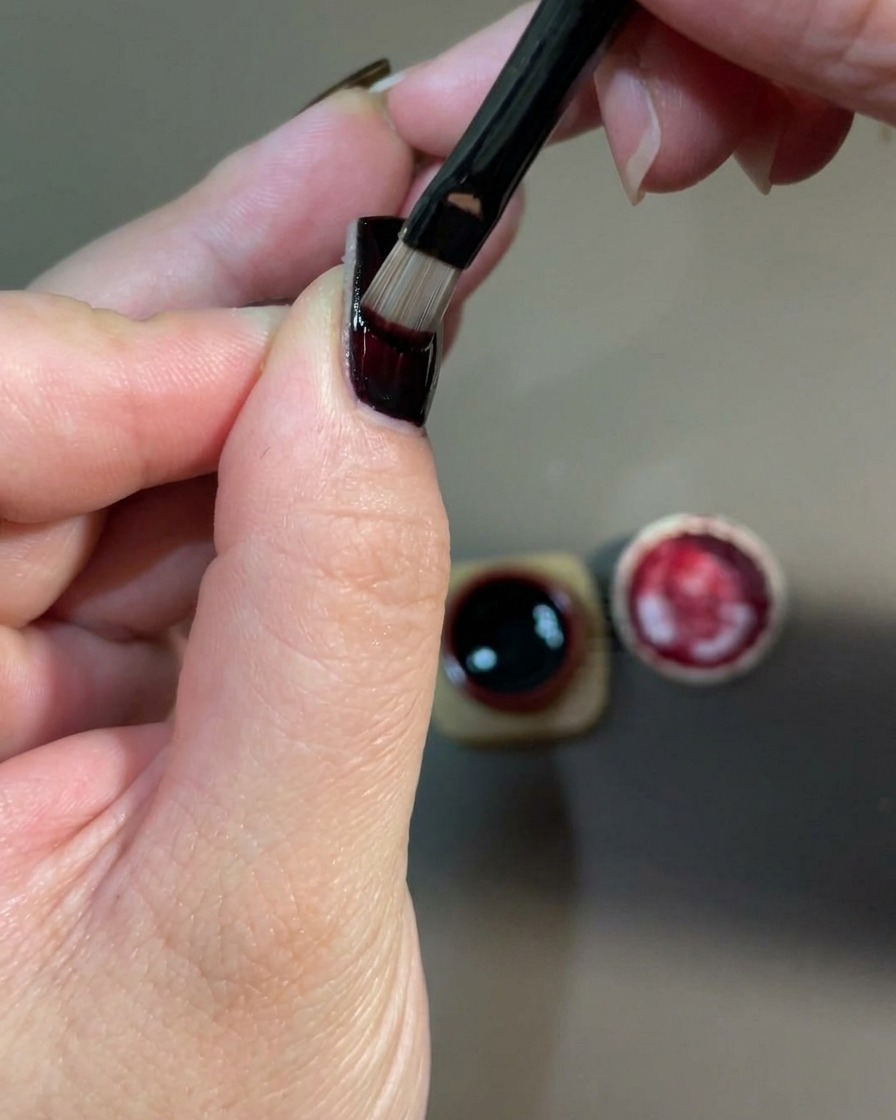 A close-up of a hand placed inside a UV nail lamp to cure the freshly applied red gel layer.