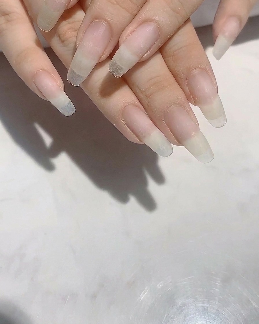 A pair of hands with long, shaped natural nails being refined with a nail file.