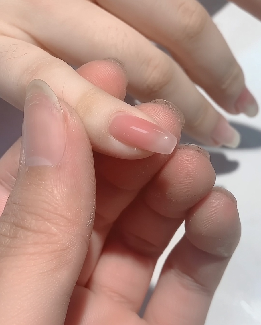 A close-up view of an applicator applying iridescent powder to the tip area of a polished nail.