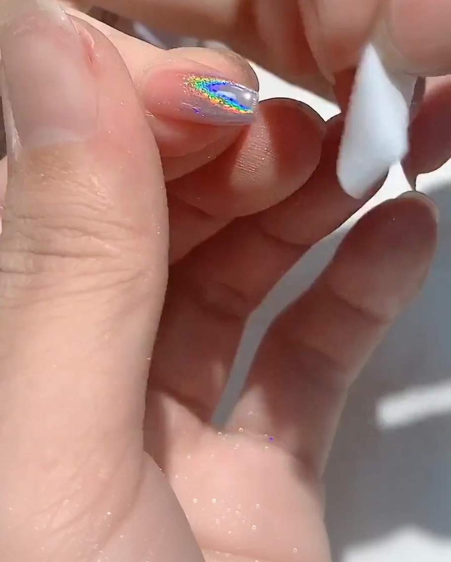 A lint-free wipe cleaning the edge of a fingernail.