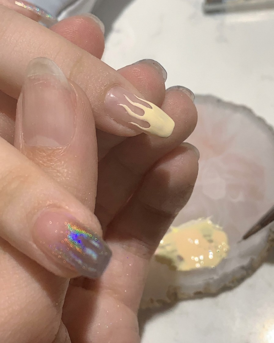 A small flat brush filling in a peach-colored flame design on a manicured nail.