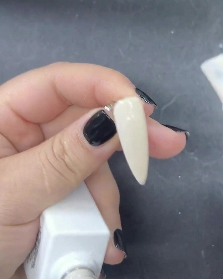 A close-up view of a brush applying a sheer milky white gel polish onto a nail.