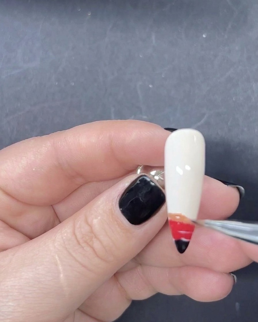 A fine liner brush adding an orange stripe of gel polish to the gradient sequence on the nail.
