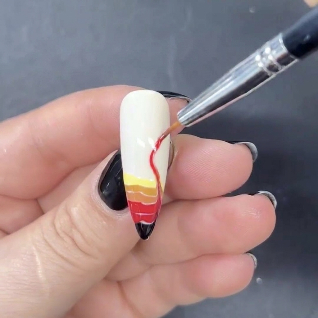 A fine liner brush being used to drag the horizontal stripes of colored gel upwards into S-shaped flame designs.